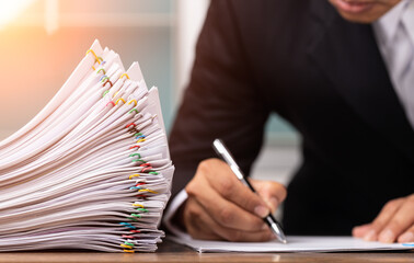 Male office workers holding and writing documents on office desk with light fair, Stack of business overload paper and paperless concept.
