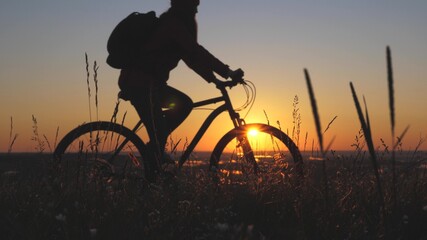 The silhouette of cyclist traveler rides along the edge of the mountain, admiring the landscape and the sunrise. Free tourist rides a bike in nature in the sun. Sports lifestyle. Cyclist exercising