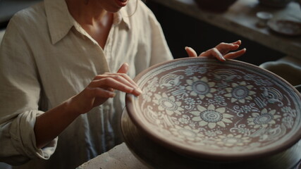 Smiling ceramist touching clay plate in workshop. Girl looking on clay product