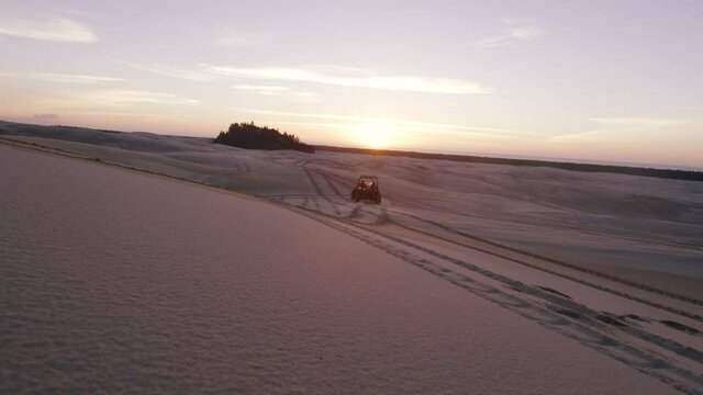 ATV four wheeler side by side drives across a sand dune at sunset
