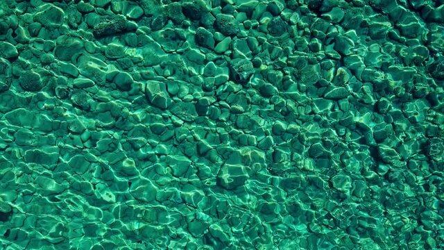 Marine abstract background with round pebbles seabed, shivering sea surface and clean transparent water