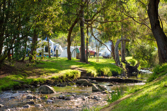 The beautiful riverbank of a small flowing river with some camping tents and fire pits in the background. Concept of outdoor adventure, family holiday, and summer fun. Great Ocean Road, Australia