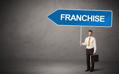 Young business person in casual holding road sign with FRANCHISE inscription, new business...