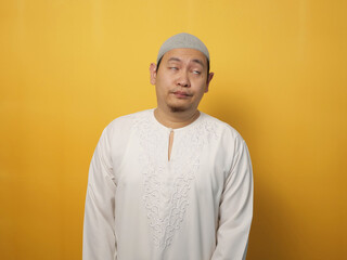 Obraz premium Portrait of young funny attractive Asian muslim man showing lazy disgust unhappy bored mocking expression, against yellow