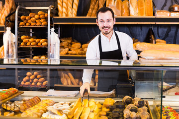 Smiling man seller showing warm tasty bun in bakery