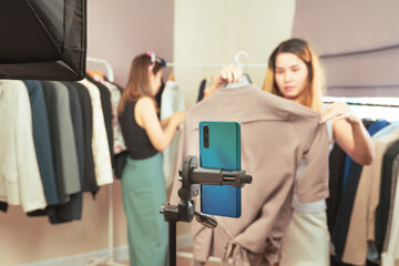 Young asian female boutique fashion owner streaming live video through a smartphone showing her new...