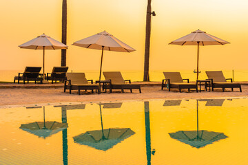 Umbrella and chair around outdoor swimming pool with sea beach ocean at sunset