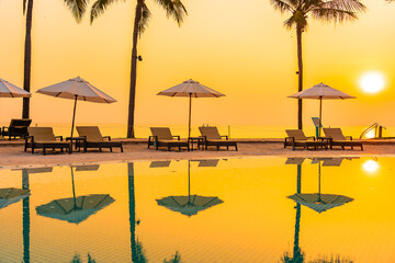 Umbrella and chair around outdoor swimming pool with sea beach ocean at sunset