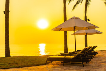 Umbrella and chair around outdoor swimming pool with sea beach ocean at sunset