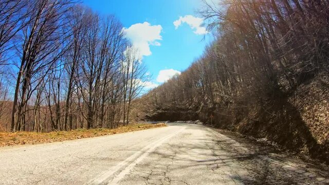 POV driving across beautiful winter landscape, bare trees forest and flickering sun blue sky, curvy asphalt mountain road, car travel gopro point of view