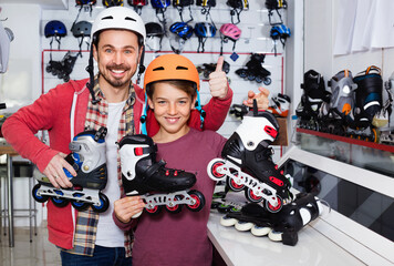 Young happy cheerful father and son showing roller-skates they bought in sports store