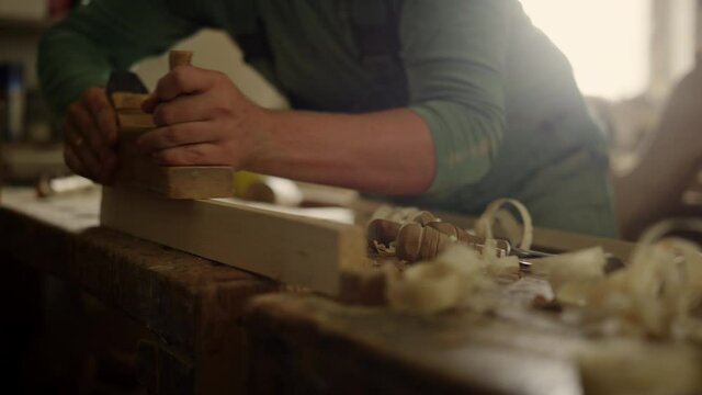 Unknown carpenter using plane in workshop. Craftmaster hands preparing plank 