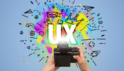 Close-up of a hand holding digital camera with abstract drawing and UX inscription
