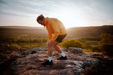 Handsome young athlete holding knee while feeling pain in knee while running in nature