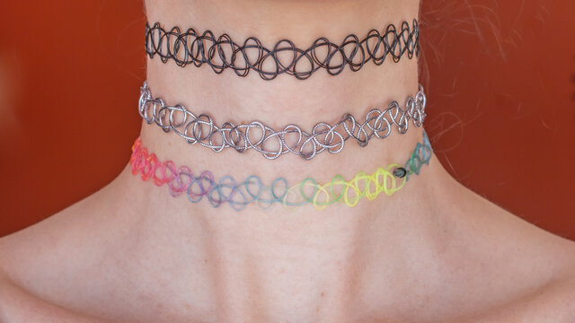 Black, silver, and rainbow multi-coloured nineties style chokers on a white woman's neck, Ontario, Canada, 2021