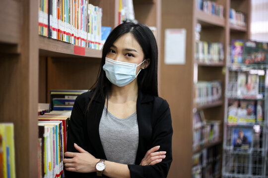 Beautiful Asian Librarian Woman  Wear Face Masks  To Prevent Coronavirus, Or COVID-19 New Normal Lifestyle In The Library.