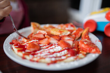 Pancake with strawberry slices and syrup on a white plate