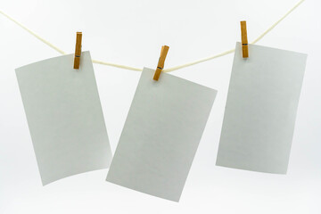 Multiple empty paper sheet for notes that hang on a rope with clothespins and isolated on white. Blank white photo hanging on rope concept