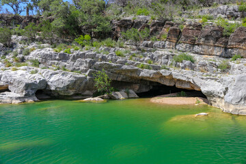 Fototapeta na wymiar Emerald green geological rock pools of water flow into a shallow limestone canyon wall creating a smaill cave in Pedernales Falls State Park Texas 