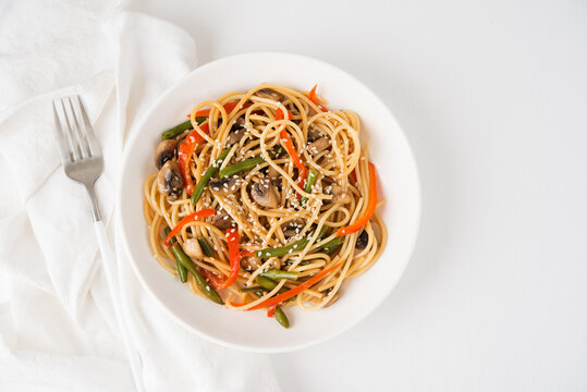 Noodles with vegetables (string beans, bell peppers, sesame seeds) and mushrooms in soy sauce, traditional Asian food, top view
