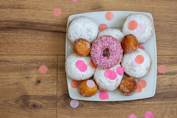 Berliner in verschiedenen Größen und Donuts auf einem weißen eckigen Teller. Alles schön zum Karneval mit Confetti dekoriert.
