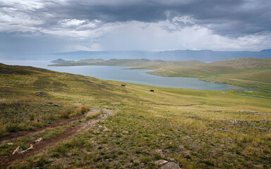 Fototapeta na wymiar View of the bay and steppes with a heavy sky Three cars driving off-road Beautiful scenery