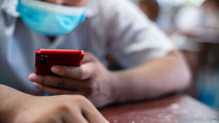 Uniform students are study online  or test exam by using smartphone and wearing protective facemask in classroom