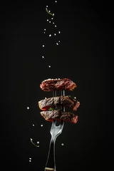 Fototapete Rund Traditional American barbecue dry aged flank steak sliced on a fork adding rosemary and sea salt in a freeze motion on black background. vertical image, American cuisine © Надія Коваль