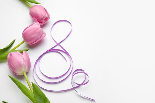 Figure 8 made of violet ribbon and tulip flowers on light background. International Women's Day celebration