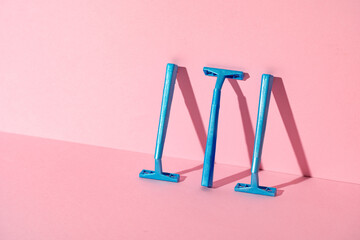 Blue disposable razors on pink paper background