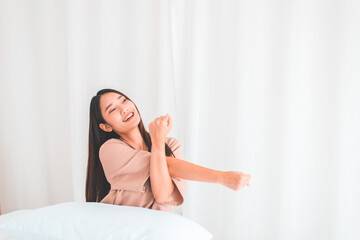Happy young asian woman stretching and waking up in her bedroom at home in the morning