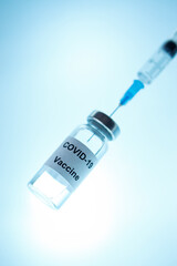 Vial of Covid-19 vaccine with syringe  on  luminous blue  background .  Vertical.