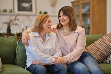 middle aged female visiting her mother, sitting together on comfortable couch, having good conversation. Woman in her forties talking to daughter at home