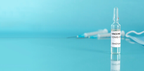 Coronavirus vaccine vial banner. Covid vaccination with vaccine ampoule and syringe. Blue background. Copy space.
