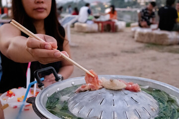 Fototapeta na wymiar Asian woman using chopsticks to roast meat, vegetables and broth Thai is called pork pan - moo kra ta.