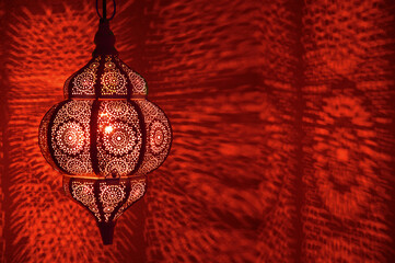 Moroccan lamp with red illuminating patterns of light on textured wall in horizontal position.