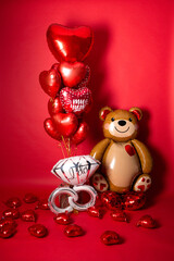 A large foil bear and a set of balloons in the form of hearts for Valentine's Day on a red background. Inscriptions in Russian balloons: "You are a miracle".