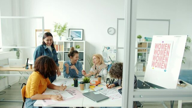 Smart active women are busy drawing gender equality banners and talking indoors in feminists office. Communication and feminism movement concept.