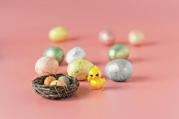 Easter eggs in a natural nest with bird eggs. Painted eggs and a decorative chicken on a pink background of pastel colors. Selective focus