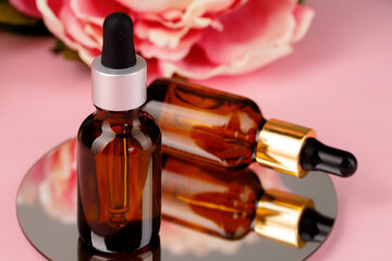 Glass bottle with oil on round mirror on pink background