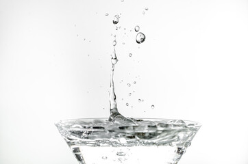 Close-up of water drop falling into a glass on white background