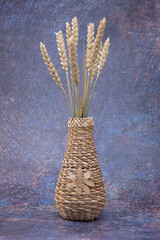 A wicker vase with a flower, with spikelets of wheat, on a dark mottled background