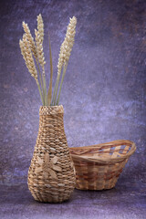 A wicker vase with a flower, with spikelets of wheat, and balls of rattan, on a dark mottled background