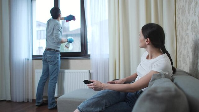 Husband washes the window and wife watches tv