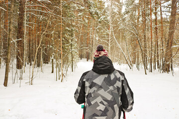 Fototapeta na wymiar Man goes in for winter sports - nordic walking, walks with sticks through a snowy forest. Active people in nature.