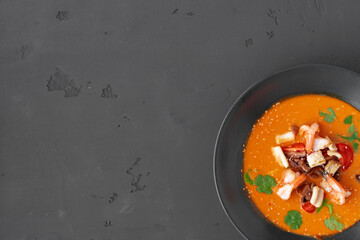 Tom yam Thai soup in black bowl served on gray background