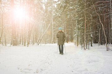 Woman goes in for winter sports - nordic walking, walks with sticks through a snowy forest. Active people in nature.