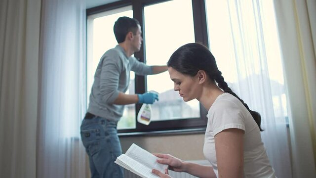 Husband cleans the window and wife reading the book
