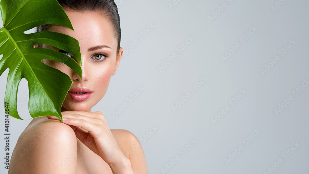 Wall mural beautiful woman with green leave near face and body. closeup girl's face with green leave. skin care