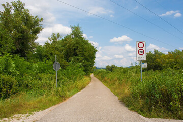 A sign on a country lane indicates that only cycles, tractors, horses and service vehicles may enter, and they must stay below 20 kph. A smaller sign indicates distances to nearby villages. In Friuli-